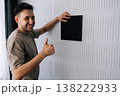 Portrait of cheerful handyman man installing a black acoustic panel on a soundproof wall, creating a modern interior design for home sound insulation and noise reduction from reverberation. 138222933