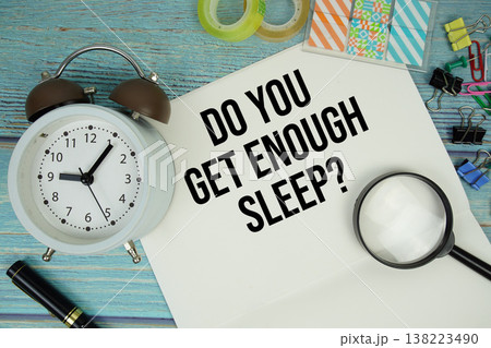 Do You Get Enough Sleep? text on a paper surrounded by office supplies, a magnifying glass, and a clock on a blue wooden surface Do You Get Enough Sleep? text on a paper surrounded by office supplies, a magnifying glass, and a clock on a blue wooden surface 138223490