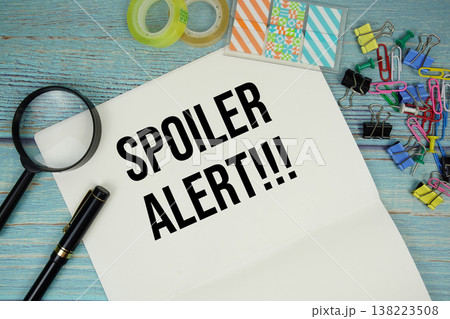 Spoiler Alert text on a paper surrounded by office supplies and magnifying glass on a blue wooden surface Spoiler Alert text on a paper surrounded by office supplies and magnifying glass on a blue wooden surface 138223508