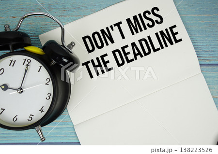 Notepad on a blue wooden table with the words "Don't Miss The Deadline" and alarm clock Notepad on a blue wooden table with the words "Don't Miss The Deadline" and alarm clock 138223526