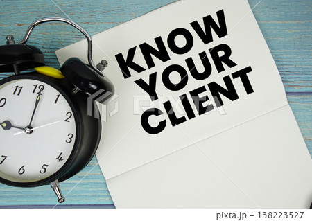 Notepad on a blue wooden table with the words "Know Your Client" and alarm clock Notepad on a blue wooden table with the words "Know Your Client" and alarm clock 138223527