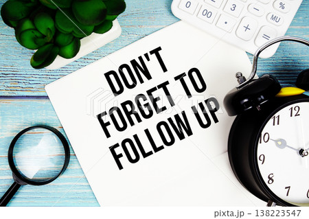 Don't Forget To Follow Up written on paper placed on a blue wooden surface, alongside a magnifying glass, a clock, a calculator, and a small plant Don't Forget To Follow Up written on paper placed on a blue wooden surface, alongside a magnifying glass, a clock, a calculator, and a small plant 138223547