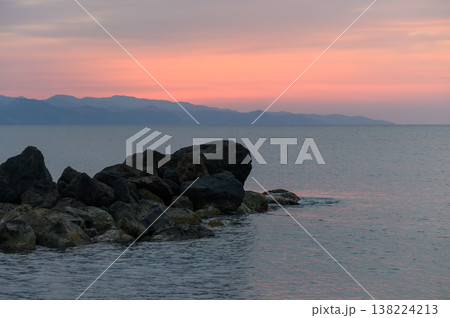 Sunset hues dance across tranquil waters by rocky shores in a serene coastal escape Sunset hues dance across tranquil waters by rocky shores in a serene coastal escape 138224213