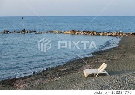 Lone lounge chair by calm sea creates serene atmosphere at twilight on a peaceful beach 138224770