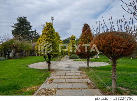 Strolling through a serene garden path lined with beautifully shaped trees under a cloudy sky in early springtime Strolling through a serene garden path lined with beautifully shaped trees under a cloudy sky in early springtime 138224780