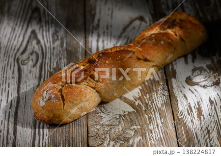 Rustic loaf of artisan bread resting on weathered wooden table in soft lighting Rustic loaf of artisan bread resting on weathered wooden table in soft lighting 138224817