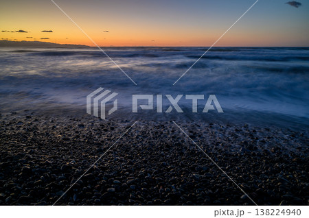 Waves gently lap the rocky shore as dusk settles over the tranquil ocean landscape 138224940