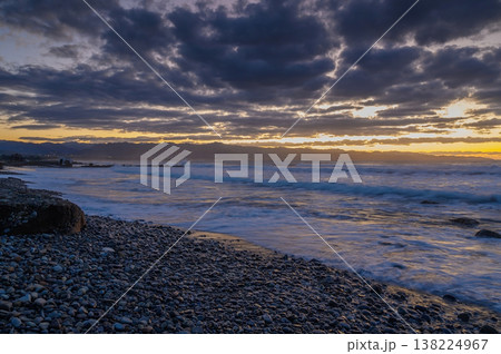 Turbulent waves and dramatic clouds embrace the sunset on a rocky shoreline Turbulent waves and dramatic clouds embrace the sunset on a rocky shoreline 138224967