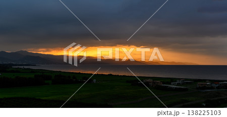 Golden sunset paints the sky over distant mountains and a tranquil sea 138225103