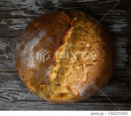 Freshly baked sourdough loaf resting on dark wooden surface with rustic charm 138225203