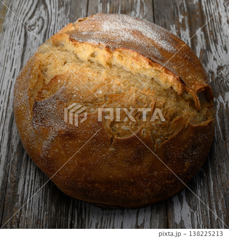 Freshly baked round loaf resting on rustic wooden surface with warm golden crust Freshly baked round loaf resting on rustic wooden surface with warm golden crust 138225213