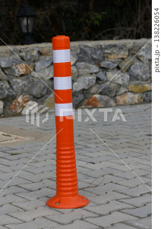 Bright orange traffic cone stands on patterned pavement near a rugged stone wall under soft natural light 138226054