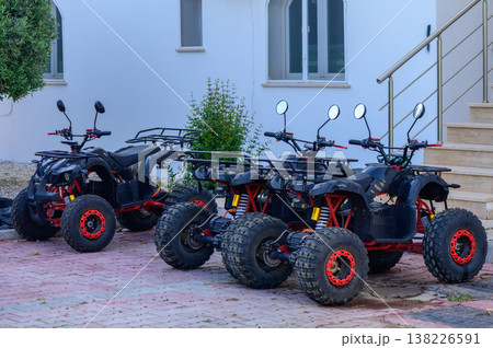 Three powerful black quad bikes parked side by side on a sunny day, ready for off-road adventure and travel. Three powerful black quad bikes parked side by side on a sunny day, ready for off-road adventure and travel. 138226591
