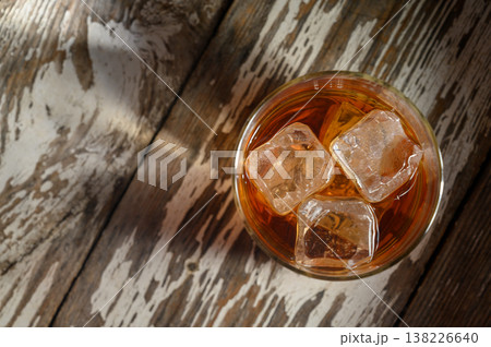 Refreshing drink with ice cubes resting on rustic wooden surface during golden 138226640