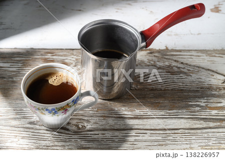 Enjoying a warm cup of coffee brewed in a shiny pot on a rustic wooden table in the morning sunlight Enjoying a warm cup of coffee brewed in a shiny pot on a rustic wooden table in the morning sunlight 138226957