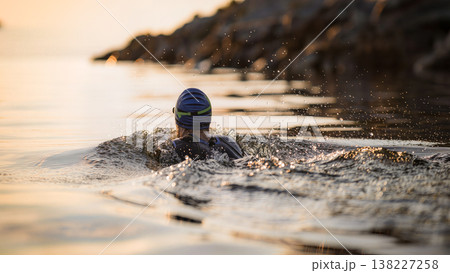 Swimmer in cap swimming in calm sea near rocky shore at sunset. Suitable for banner, sports article, fitness, triathlon, or website design. 138227258