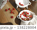 Fresh organic strawberries on wooden board and vintage ceramic bowls. Trendy rustic kitchen scene with red berries, white colander and sunlight shadows for healthy cottagecore lifestyle. 138228004