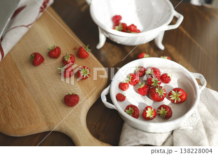 Fresh organic strawberries on wooden board and vintage ceramic bowls. Trendy rustic kitchen scene with red berries, white colander and sunlight shadows for healthy cottagecore lifestyle. Fresh organic strawberries on wooden board and vintage ceramic bowls. Trendy rustic kitchen scene with red berries, white colander and sunlight shadows for healthy cottagecore lifestyle. 138228004