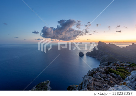 Scenic view of Mallorca northwest coastline at sunrise with rugged cliffs, calm Mediterranean Sea, distant horizon, and soft clouds lit by early morning light 138228357