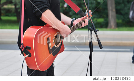 Street musician playing acoustic guitar outdoors, performing live music for passersby 138228456