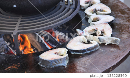 Fish steaks cooking on round grill over open fire Fish steaks cooking on round grill over open fire 138228560