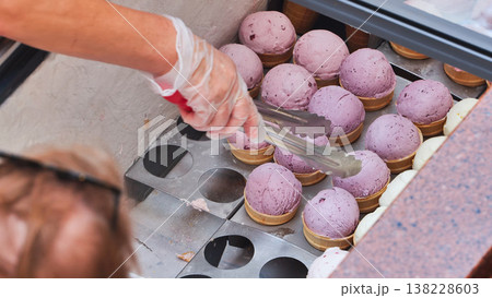 Serving blueberry ice cream scoops in waffle cones from a shop freezer Serving blueberry ice cream scoops in waffle cones from a shop freezer 138228603