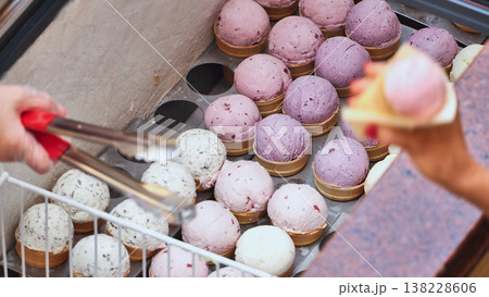 Seller serving various flavors of ice cream cones from display freezer Seller serving various flavors of ice cream cones from display freezer 138228606