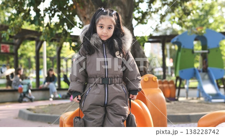 Young girl playing on playground wearing warm winter jumpsuit Young girl playing on playground wearing warm winter jumpsuit 138228742