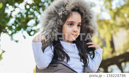 Young girl wearing fur hood winter jacket in bright autumn park light 138228786