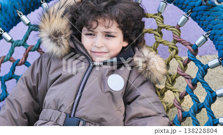 Little boy resting in colorful rope nest swing enjoying childhood leisure at playground Little boy resting in colorful rope nest swing enjoying childhood leisure at playground 138228804