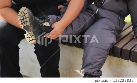 Mother helping child put on warm winter boot outdoors, demonstrating care and parenting Mother helping child put on warm winter boot outdoors, demonstrating care and parenting 138228833