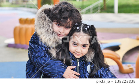 Siblings sharing a warm hug and connection, playing at the park in winter coats Siblings sharing a warm hug and connection, playing at the park in winter coats 138228839