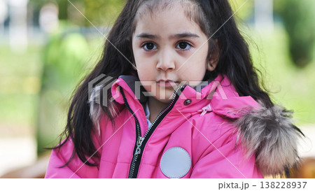 Young girl looking forward in pink winter coat portraying childhood innocence Young girl looking forward in pink winter coat portraying childhood innocence 138228937