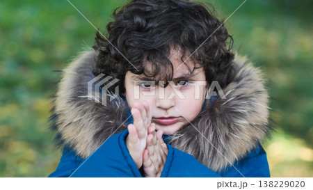 Young boy feeling cold and warming his hands outdoors in a fur hood coat 138229020