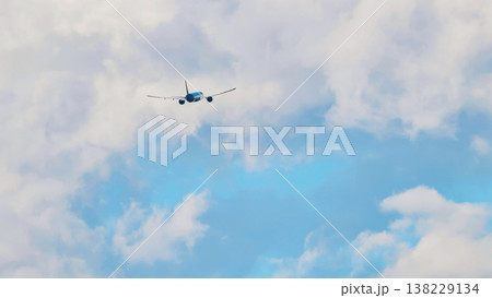 Passenger airplane flying away through white clouds in a blue sky 138229134
