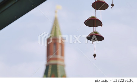 Decorative hanging bells with a historic tower blurred in the background against a pale sky. Decorative hanging bells with a historic tower blurred in the background against a pale sky. 138229136