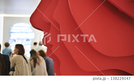 Abstract red sculpture creating layered profiles with people viewing art exhibition 138229147