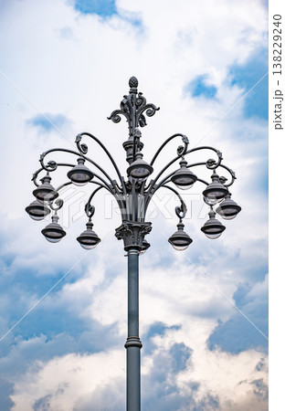 Ornate street lamp illuminating urban evening sky with complex ironwork details Ornate street lamp illuminating urban evening sky with complex ironwork details 138229240