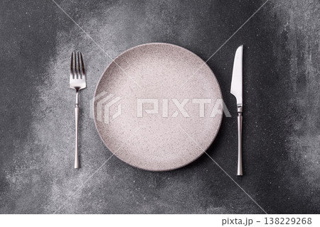 An empty round ceramic plate, knife, and fork as a dining table setting. An empty plate 138229268