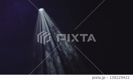 Theatrical spotlight shines through smoke on a dark stage background Theatrical spotlight shines through smoke on a dark stage background 138229422