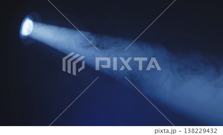 Blue spotlight beam shining through dense smoke on a dark stage. Theatrical lighting effect. Blue spotlight beam shining through dense smoke on a dark stage. Theatrical lighting effect. 138229432