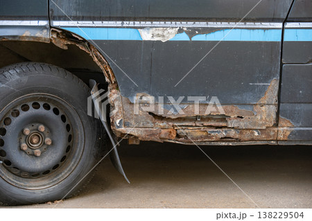 Car body rusting and decaying, showing corrosion on old metal vehicle door and wheel arch 138229504