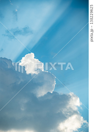 Blue sky background with white cumulus clouds, bright sunbeams streaking through 138229625