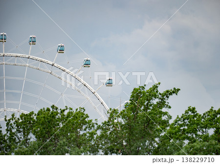 Ferris wheel cabins against cloudy sky above green trees in amusement park 138229710