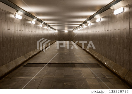 Empty underground pedestrian tunnel illuminated by multiple lights creating a vanishing point Empty underground pedestrian tunnel illuminated by multiple lights creating a vanishing point 138229755