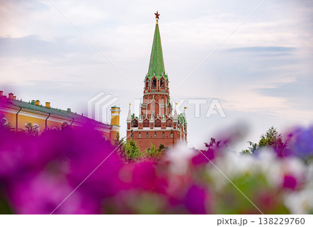 Kremlin's Troitskaya Tower rising above colorful flowers against a cloudy sky 138229760