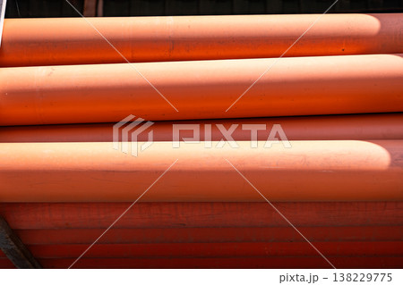 Stacked orange PVC pipes creating an abstract pattern with light and shadow 138229775
