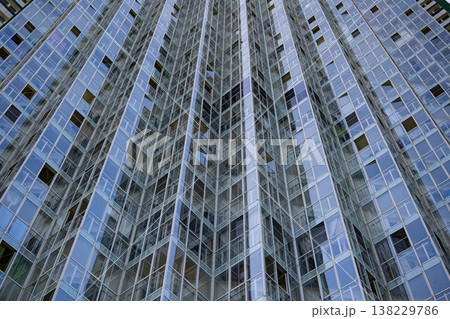Modern skyscraper facade with repeating glass panels and geometric blue reflections 138229786