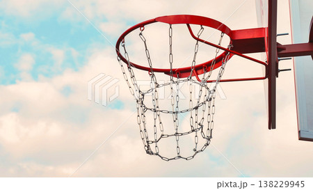 Red basketball hoop with a metal chain net against a cloudy blue sky. 138229945