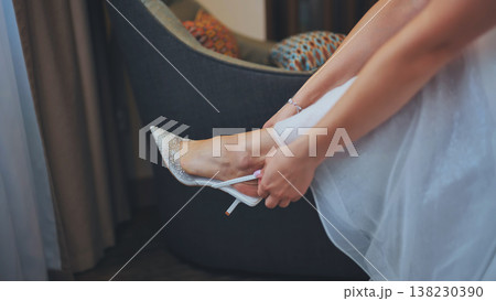 Bride putting on elegant high heel shoes before wedding ceremony. 138230390